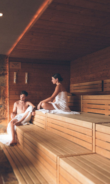 Paar sitzt auf den Stufen der Finnischen Sauna und entspannt in der Saunawelt des Hotel Eibl-Brunner.