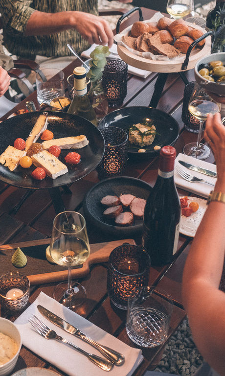 Gäste teilen sich die Vielfalt an Gerichten und Speisen die auf dem Tisch im Garten des Hotel Eibl-Brunner stehen.