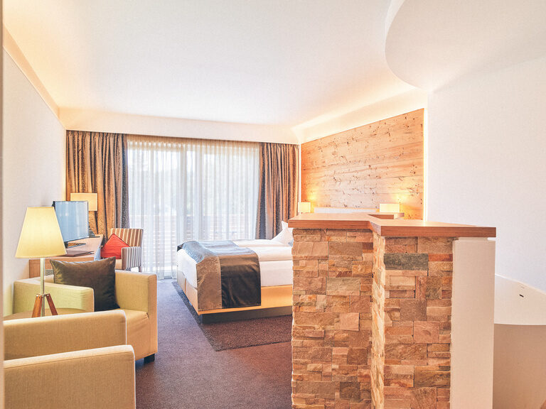 Doppelzimmer Arber im Hotel Eibl-Brunner - Blickrichtung Balkon mit Sitzgelegenheit und Doppelbett im Blick.
