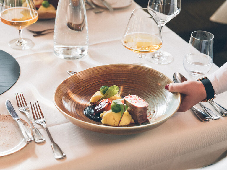 Ein für mehrere Gänge gedeckter Tisch, mit Weingläsern, Besteck und Brot mit Butter, im Restaurant Hotel Eibl-Brunner.