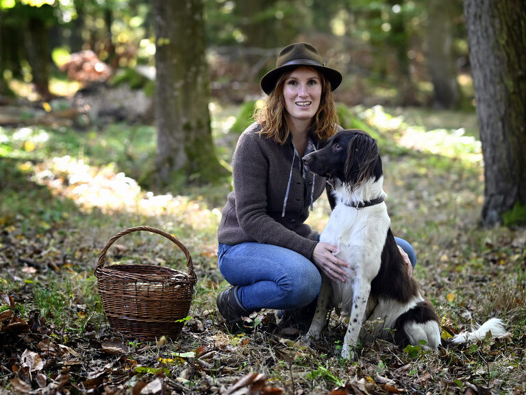 Försterin und Wald- & Kräuterpädagogin Lena Konofsky im Wald mit Ihrem Hund und einem Korb.