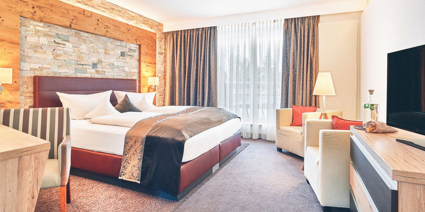 Hotel Zimmer im Wellnesshotel Eibl-Brunner mit roten Bett, Schreibtisch, Balkon und Sitzgelegenheiten.