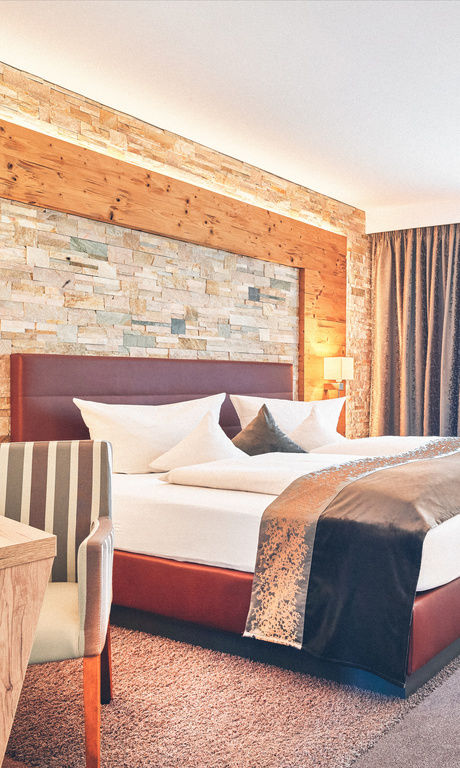 Hotel Zimmer im Wellnesshotel Eibl-Brunner mit roten Bett, Schreibtisch, Balkon und Sitzgelegenheiten.
