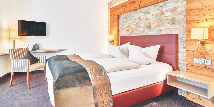Doppelzimmer mit roten Bett vor einer Stein-Holzwand im Hotel Eibl-Brunner.