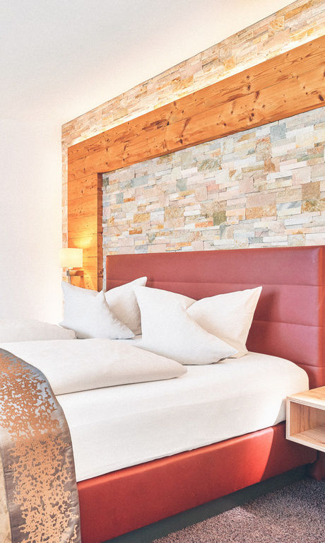 Doppelzimmer mit roten Bett vor einer Stein-Holzwand im Hotel Eibl-Brunner.
