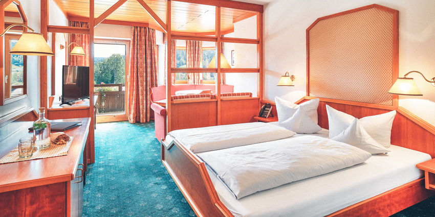 Zimmer mit Doppelbett in Holzrahmen, Sitzecke und Balkon.