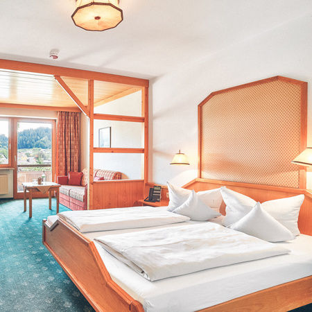 Großzügiges Familienappartement im Stammhaus des Hotel Eibl-Brunner. Gemütliches Bett, gegenüber Schreibtisch und gleich daneben Sitzecke mit Fernseher und Zugang zum Balkon.