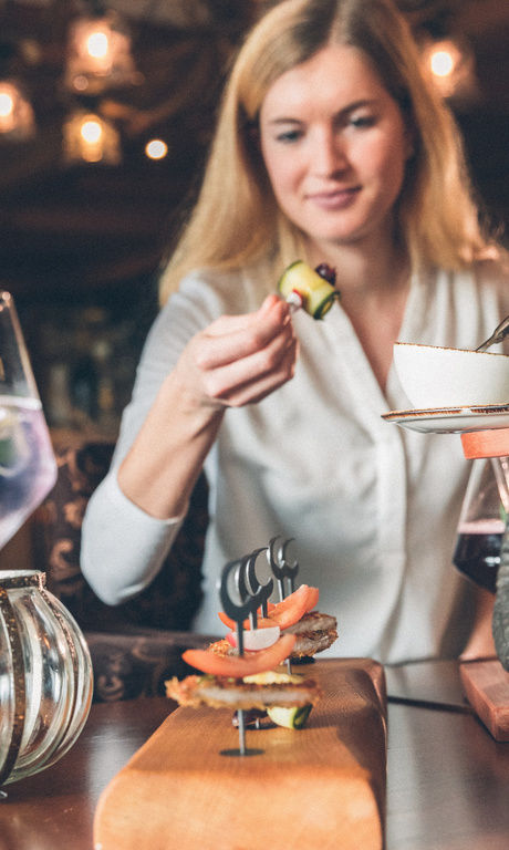 Fingerfood auf Spiesen werden zwei Gästen/innen gereicht. Gemeinsam mit zwei Getränken aus der Bar des Hotels.