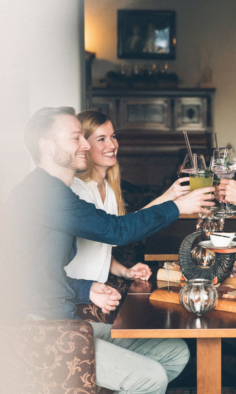 Gäste stoßen mit Getränken im Restaurant, an einem gedeckten Tisch miteinander an.