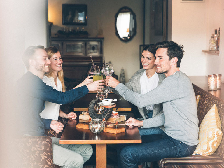 Gäste stoßen mit Getränken im Restaurant, an einem gedeckten Tisch miteinander an.