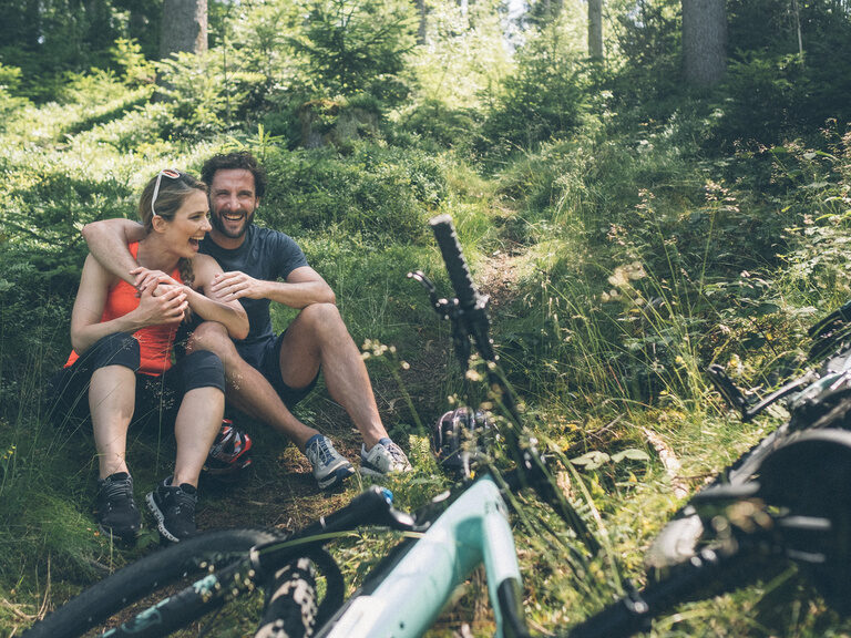 Zwei Gäste machen Pause auf Moos und Gras bei einer E-Biketour durch den Wald.