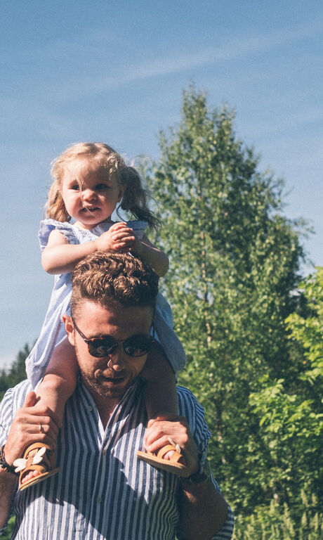 Hotelbesitzer Stefan Brunner trägt seine Tochter auf den Schultern und geht mit Ihr in der Sonne spazieren.