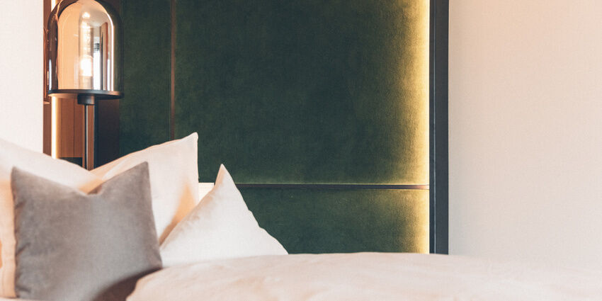 Flauschige Kissen liegen auf dem Bett und angenehmes Licht taucht das Zimmer in eine entspannende Atmosphäre.