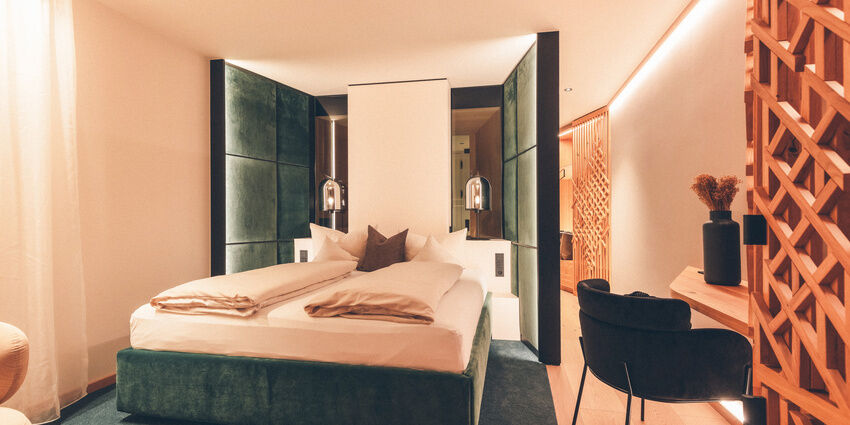 Grünes Doppelbett, vor grüner Wand und neben einem Schreibtisch im Wald Spa Studio des Hotel Eibl-Brunner, in Frauenau.