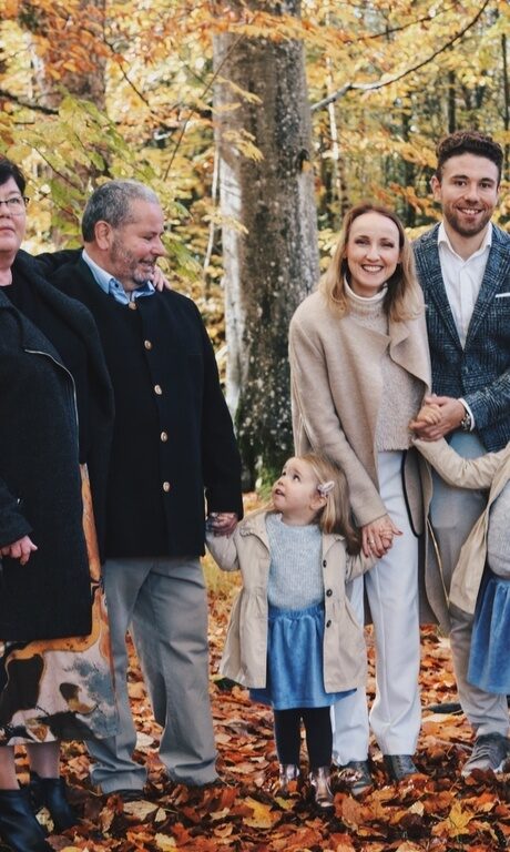 Familie Brunner - 3 Generationen mit Hund, mit herbstlich bunten Blättern auf dem Waldboden.