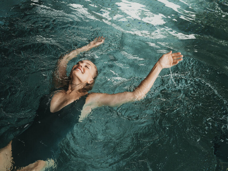 Eine Besucherin der Hotel Eibl-Brunner lässt sich glücklich auf dem Rücken im Wasser treiben.