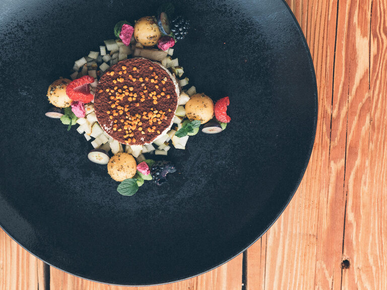 Dessert mit Kakaopulver auf Obstwürfeln, garniert mit Melonenkügelchen und Minze.