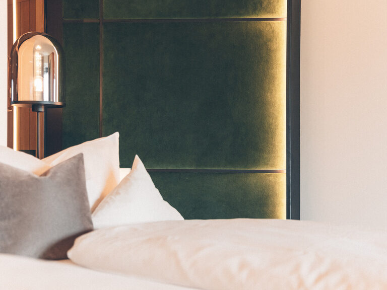 Flauschige Kissen liegen auf dem Bett und angenehmes Licht taucht das Zimmer in eine entspannende Atmosphäre.