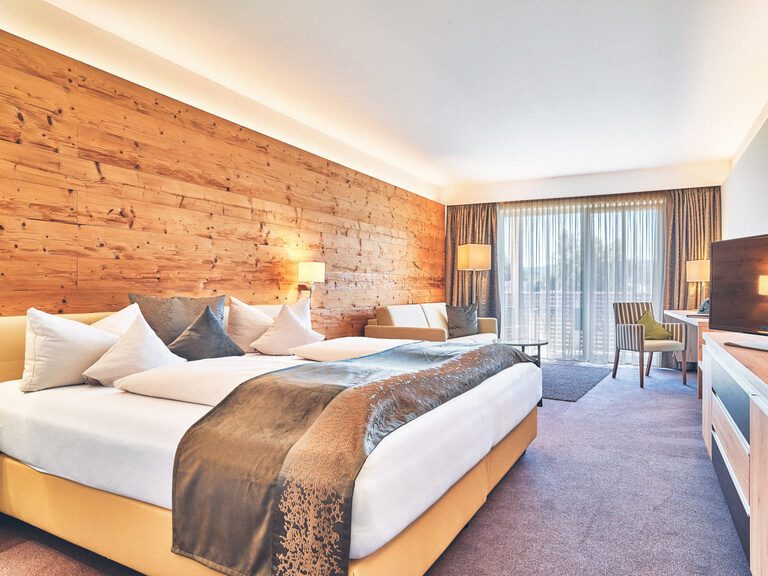 Doppelbett im Doppelzimmer Josefi mit Blick auf den Fernseher und im Hintergrund die Balkontüre nach draußen.