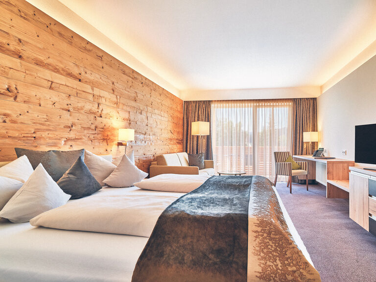 Großes Doppeluimmer mit Holzverkleidung und gemütlicher Couch, Schreibtisch und Teppichboden im Hotel Eibl-Brunner.