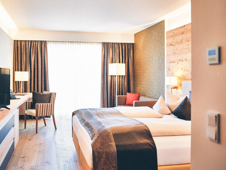 Helles Doppelzimmer mit Schreibtisch für Businessreisende, einer Doppelsitzer-Couch und Holzboden im Hotel Eibl-Brunner.