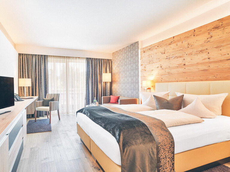 Doppelzimmer mit gemütlichen Doppelbett mit Sicht auf den Fernseher und im Hintergrund ein Schreibtisch.