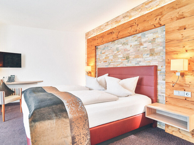 Doppelzimmer mit roten Bett vor einer Stein-Holzwand im Hotel Eibl-Brunner.