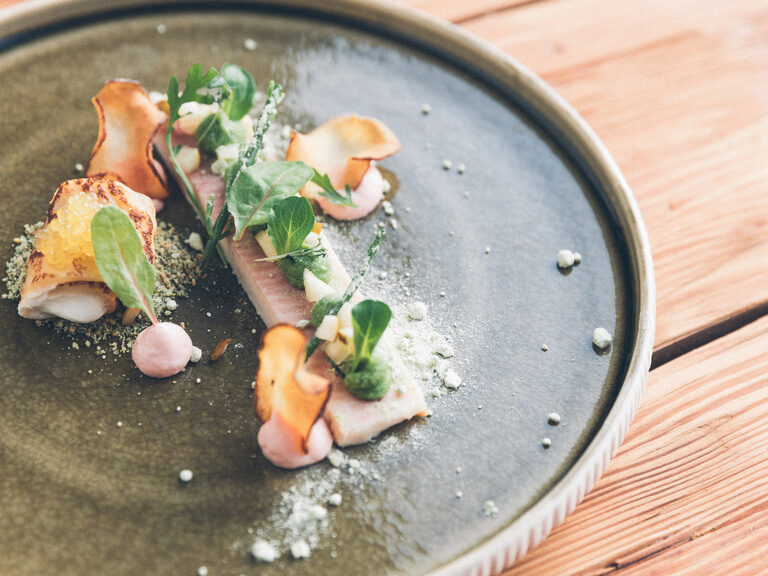 Fisch mit Gemüsechips, garniert mit Babyspinat und Kräutern.