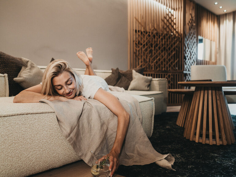 Eine junge Frau entspannt mit einem Cocktail auf einer Couch im Hotel Eibl-Brunner in Frauenau