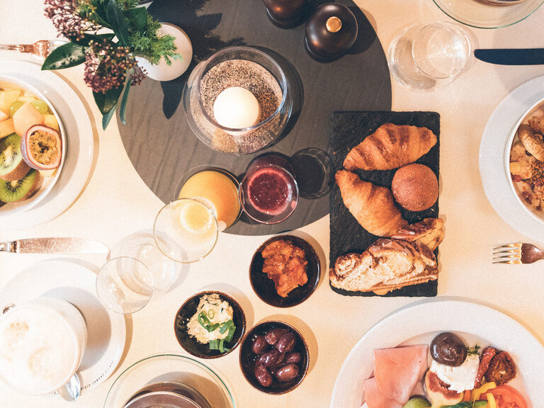 Frühstückstisch mit vielfältiger Auswahl vom Buffet mit Säften, Obst, Wurst und Käse, verschiedenes Gebäck & frischen Kaffee.