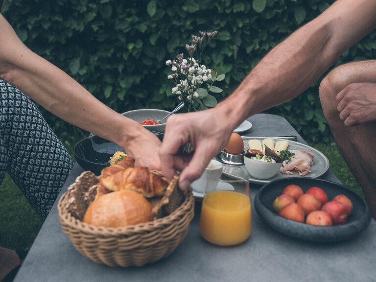 Pärchen Frühstückt gemeinsam im Garten des Hotel Eibl-Brunner mit Brötchen, Obst und Säften.