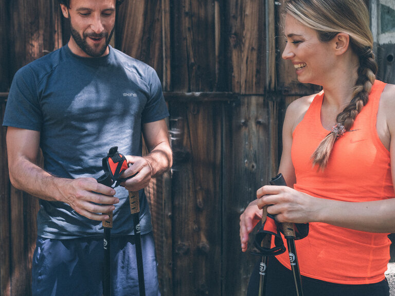 Gäste Paar vor Scheune Nordic Walking Ein Paar mit Nordic Walking Stöcken steht vor einer Holzscheune und zieht sich die Stöcke gerade wieder an.