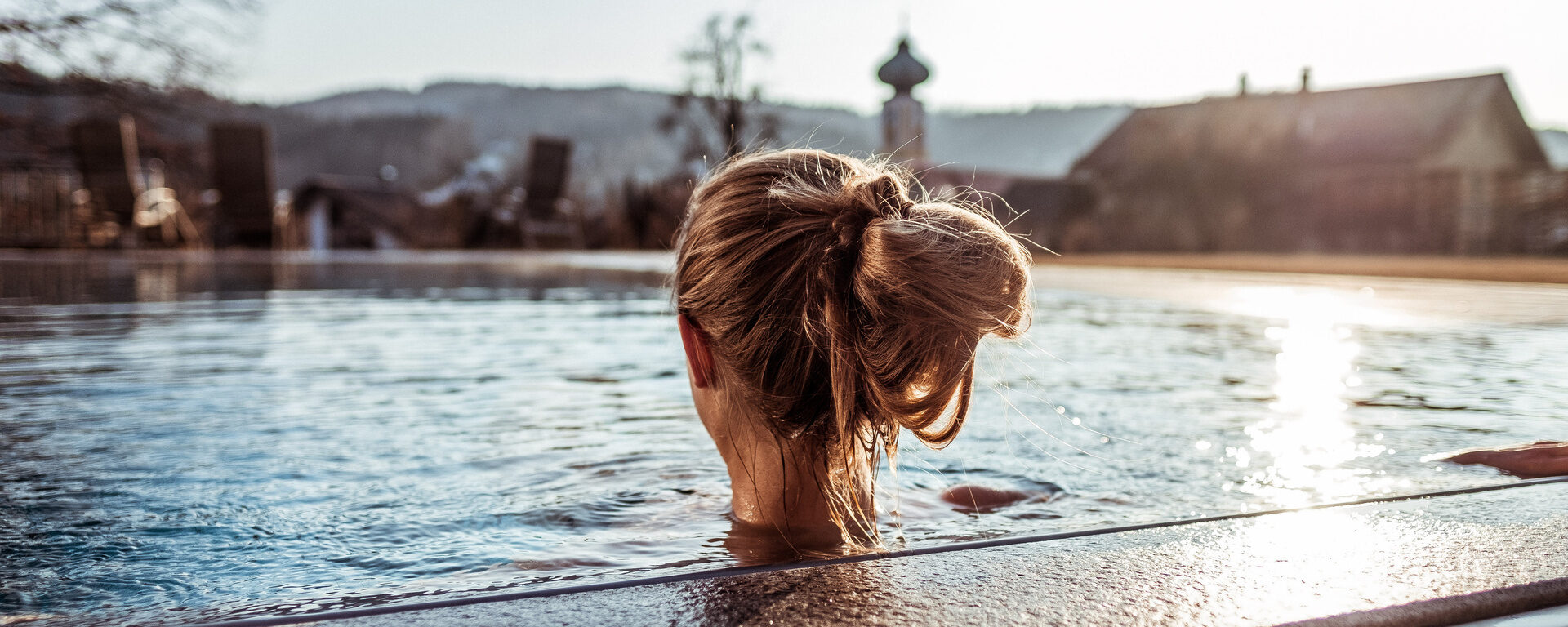 Frau genießt das Wasser im Außenpool des Hotel Eibl-Brunner und blickt auf die Sonnenliegen im Garten.