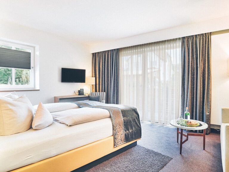 Gelbes Doppelbett in hellen Raum, auf weichen, grauen Teppich. Daneben eine zweisitzer Couch und gegenüber ein Schreibtisch.