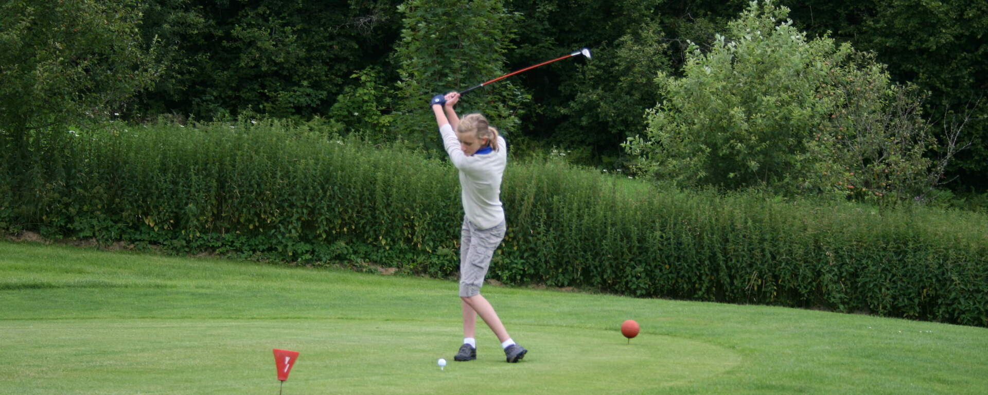 Eine golfende Frau auf dem Green die dabei ist einen Golfball mit dem Schläger zu treffen.