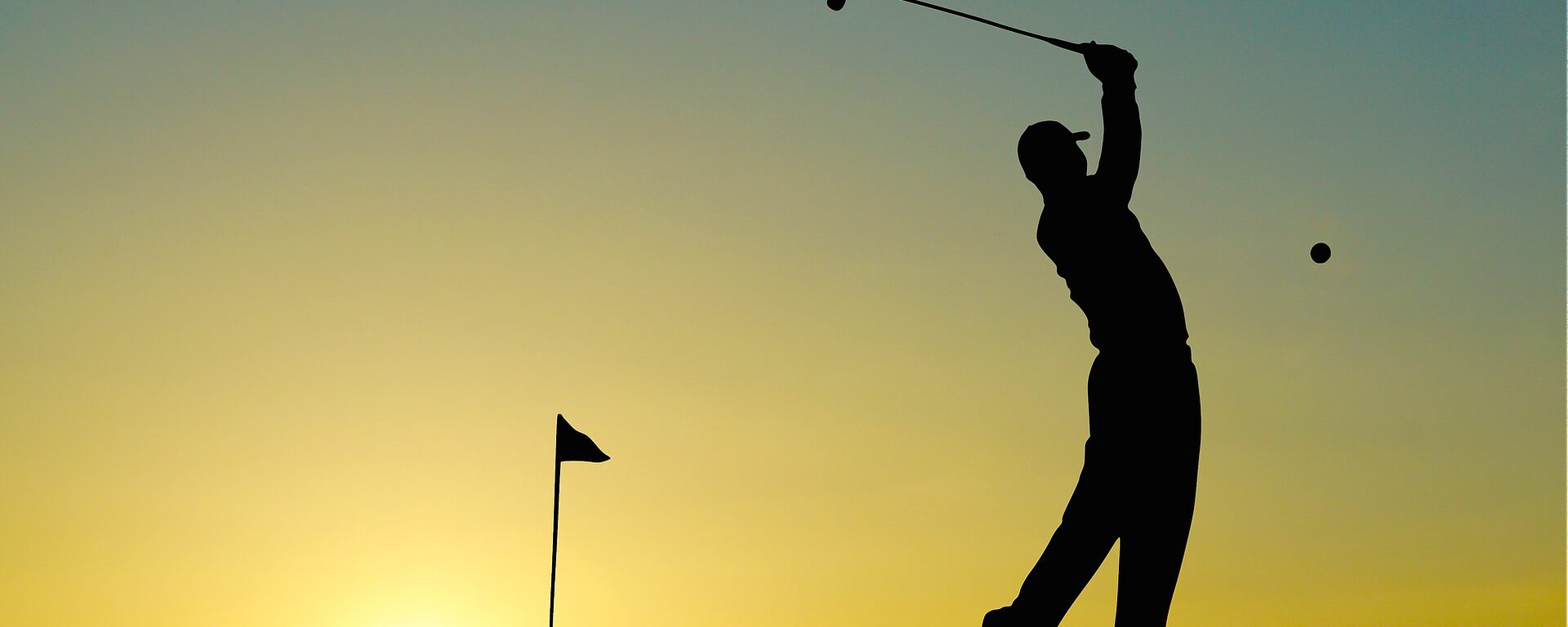 Golfer beim Schlag eines Golfballs, die Fahne im Rücken bei Sonnenuntergang.