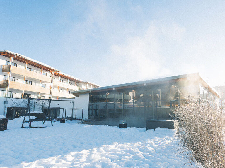 Ruhig liegt das Hotel Eibl-Brunner in Frauenau, der beheizte und im Winter dampfende Außenpool ist im verschneiten Garten