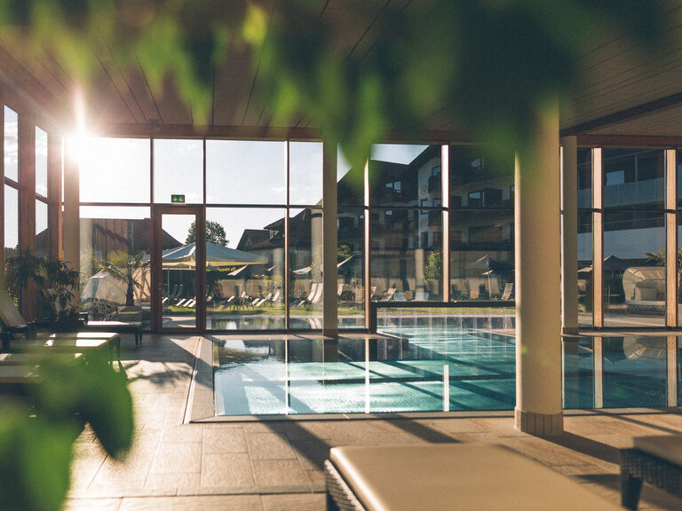 Blick über den Innenpool des Hotel Eibl-Brunner auf die Liegewiese, durch die Fensterfront mit Sonnenstrahlen.