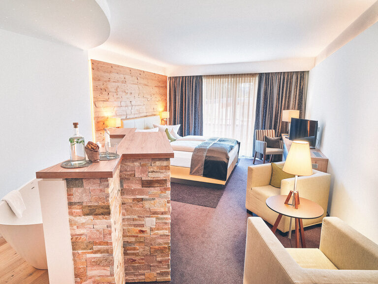 Doppelzimmer im Hotel Eibl-Brunner mit offenen Badezimmer, freistehender Badewanne und gemütlichen Sitzgelegenheiten im Raum.