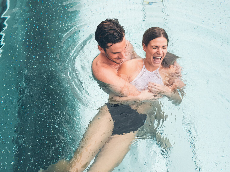 Ein Paar lacht und hat viel Spaß im Wasser des Hotelpools des Wellnesshotel Eibl-Brunner.