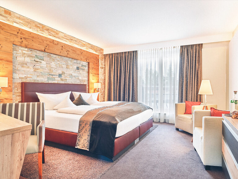 Hotel Zimmer im Wellnesshotel Eibl-Brunner mit roten Bett, Schreibtisch, Balkon und Sitzgelegenheiten.