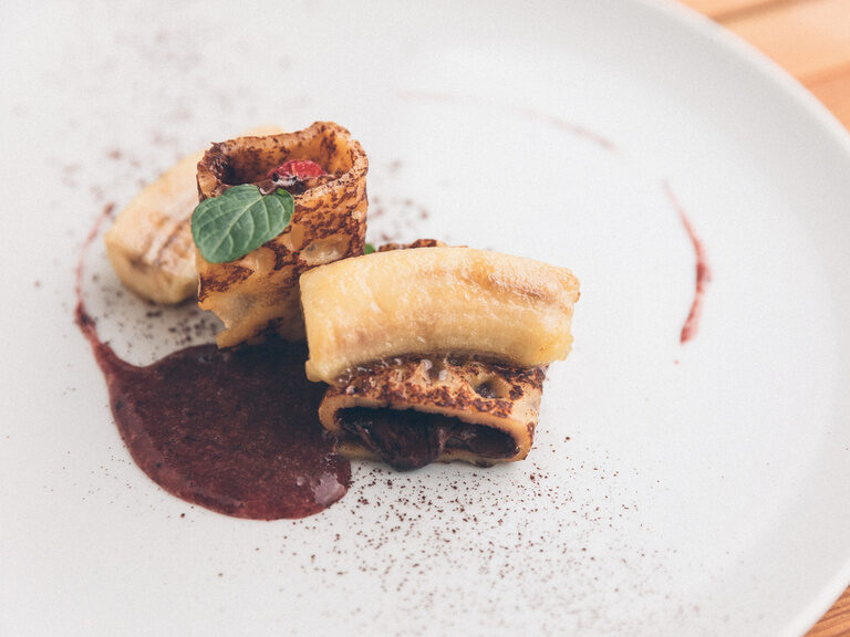 Schokoladen Pfannkuchen oder Crepe, garniert mit karamelisierter Banane auf Fruchtspiegel.