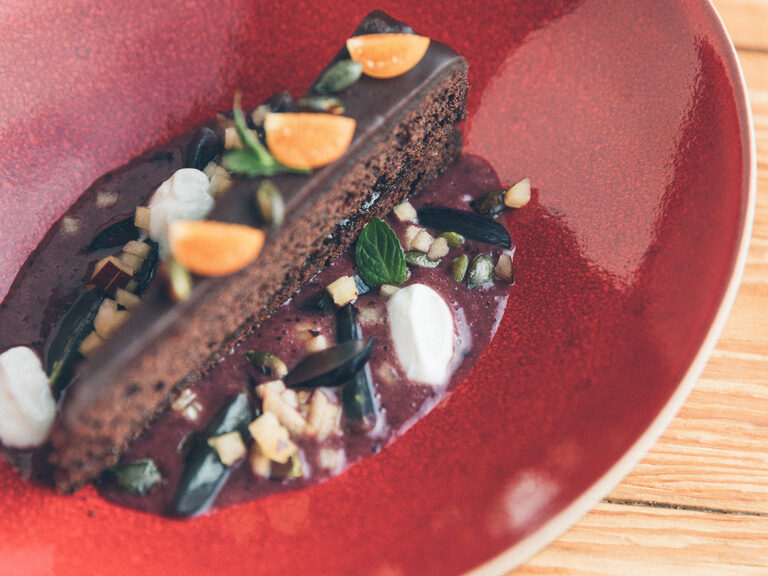 Schokoladenkuchen auf Fruchspiegel, garniert mit Früchten und Schlagsahne.