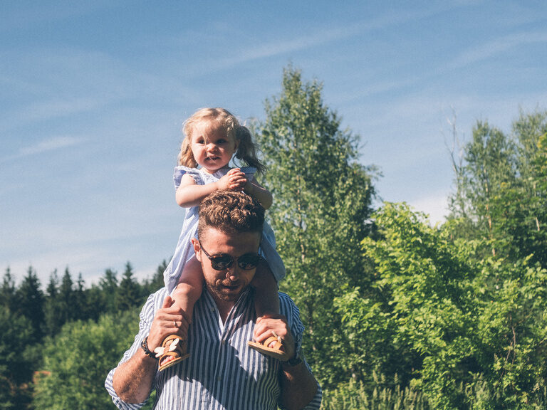 Hotelbesitzer Stefan Brunner trägt seine Tochter auf den Schultern und geht mit Ihr in der Sonne spazieren.