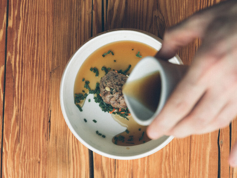 Leberknödelsupper in einer weissen Suppenschüssel in die Brühe geschüttet wird.
