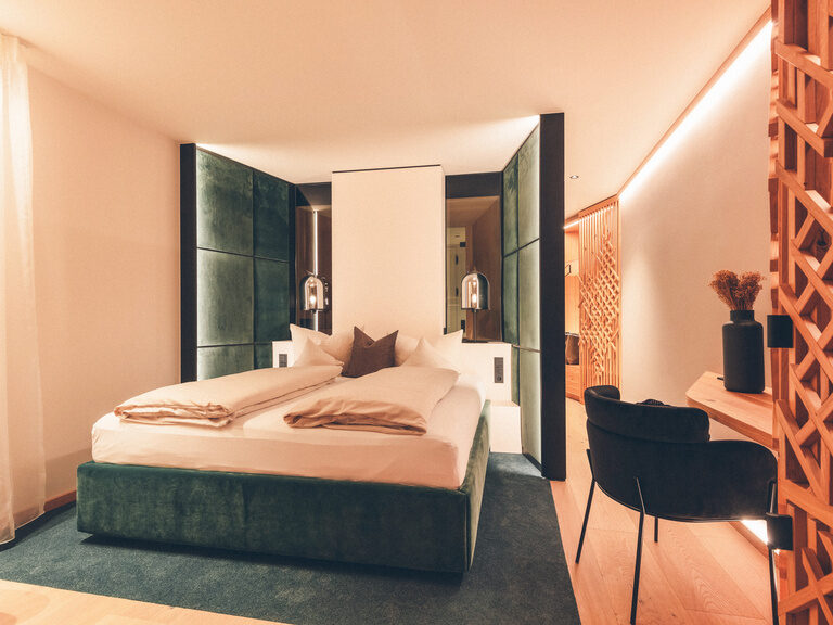 Grünes Doppelbett, vor grüner Wand und neben einem Schreibtisch im Wald Spa Studio des Hotel Eibl-Brunner, in Frauenau.