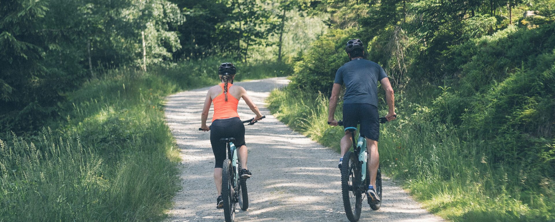 Zwei Radfahrer - zwei Gäste des Hotel Eibl-Brunner fahren durch den saftig grünen Wald in der Nähe des Hotels.