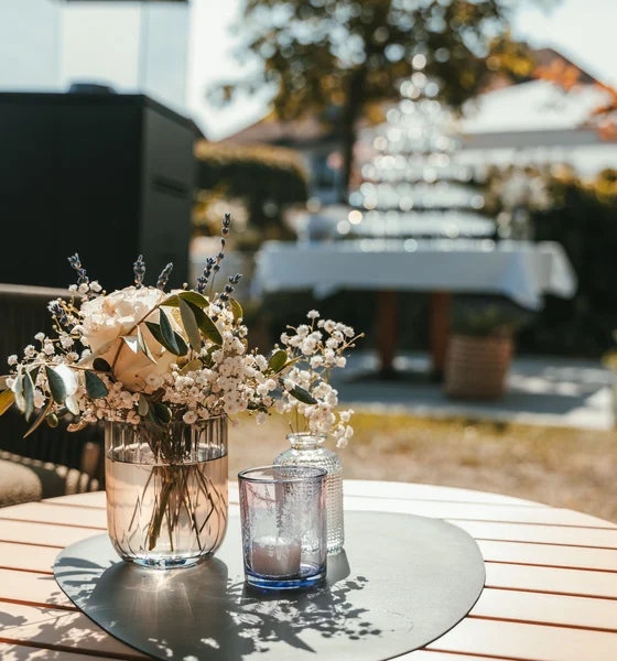 Blumendekoration und Kerzen auf rundem Holztisch im Freien bei Sonnenschein