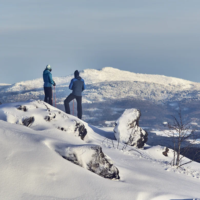 Zwei Wanderer mit Stöcken auf verschneitem Berg mit Blick auf schneebedeckte Landschaft