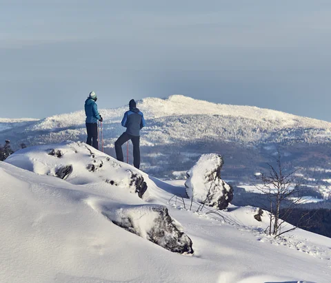 Zwei Wanderer mit Stöcken auf verschneitem Berg mit Blick auf schneebedeckte Landschaft